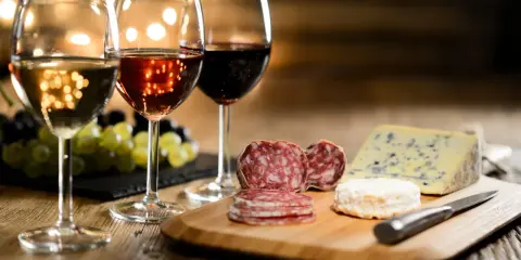 Trois verres de vin, blanc, rosé et rouge, accompagnent un plateau de fromages et charcuteries. La question est : quel vin avec le fromage ?