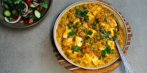 Cremiges Matar Paneer mit Erbsen und würzigen Paneer-Würfeln, garniert mit Koriander. Daneben ein frischer Salat.