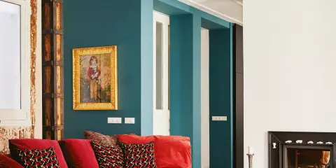 Sofá rojo vibrante con cojines estampados, pared azul petróleo y detalles rústicos. ¡Los mejores colores para pintar una casa!