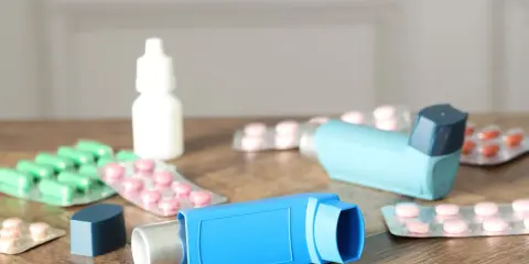 Dwa niebieskie inhalatory i opakowania leków, w tym zielone kapsułki i różowe tabletki. To zestaw na astmę, czyli oxodil combo.