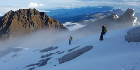 Dwóch alpinistów na ośnieżonym zboczu, w tle majestatyczne góry Ekwadoru, w tym najwyższy szczyt ekwadoru.