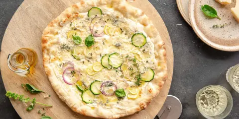 Pyszna pizza bianca z cukinią, cebulą i cytryną, podana na drewnianej desce.