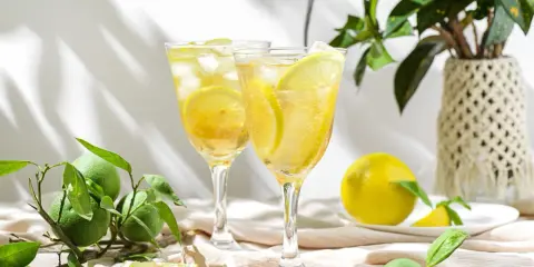 Dwa orzeźwiające drinki z lodem i plasterkami cytryny, idealne na upalne dni. Obok leżą świeże cytryny i zielone owoce.