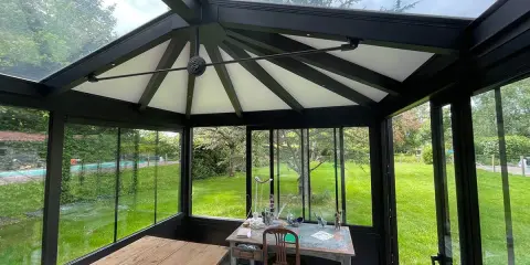 Intérieur d'une **veranda 2 pans** avec mobilier, sol décoratif et vue sur un jardin verdoyant.