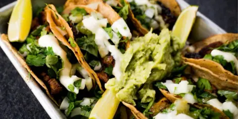 Saftige Tacos al Pastor mit Guacamole, Koriander und Limettenspalten.