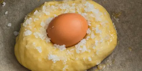Masa para receta mona de pascua esponjosa, con un huevo crudo incrustado y espolvoreada con azúcar.