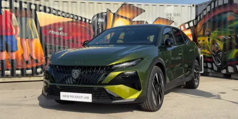 Nowy Peugeot 408 po lifcie, w kolorze zielonym, prezentuje się na tle kolorowych murali na kontenerach.