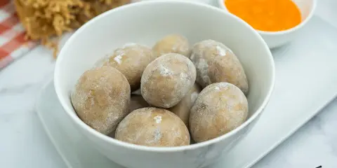 Un tazón blanco lleno de papas arrugadas, cubiertas de sal, junto a un pequeño cuenco con mojo rojo.
