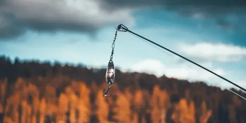 Przynęta z haczykiem wisi na żyłce, gotowa do połowu na jeziorze Skarlińskim. W tle jesienne drzewa i błękitne niebo.
