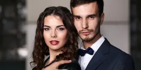 Elegancka para, niczym koziorożec i baran, pozuje do zdjęcia. Ona w ciemnej sukni, on w granatowym garniturze.
