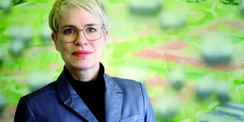 Frauke Burgdorff, eine Frau mit kurzen blonden Haaren und Brille, blickt lächelnd in die Kamera. Sie trägt einen grauen Blazer.