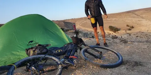 Mann mit Fahrrad und Zelt in bergiger Landschaft, bereit für neue **biking trails**.