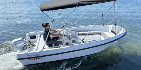 Ce bateau Terhi 450, propulsé par un moteur Honda de 6 cv, navigue sur une mer calme. Idéal pour explorer les côtes.