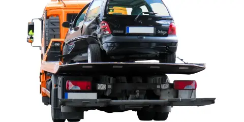Pomoc drogowa pokazuje, jak holować auto po wypadku. Uszkodzony czarny Renault Twingo jest ładowany na lawetę.