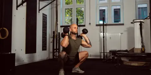 Mann macht Kniebeugen mit Kurzhanteln. Ein Supersatz ist, wenn zwei Übungen direkt hintereinander ohne Pause ausgeführt werden.