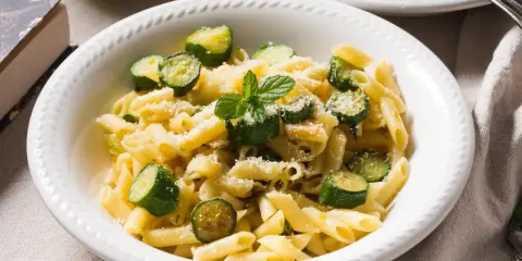 Pyszne danie z makaronem penne i kawałkami cukinii, posypane parmezanem i listkami mięty. Idealne co z cukinii na obiad!