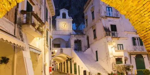Un vicolo illuminato ad Atrani, con un arco giallo in primo piano e un campanile con orologio sullo sfondo.