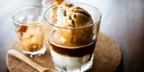 Ein italienischer Eiskaffee, Affogato, mit Vanilleeis und heißem Espresso. Ein Holzlöffel liegt daneben.