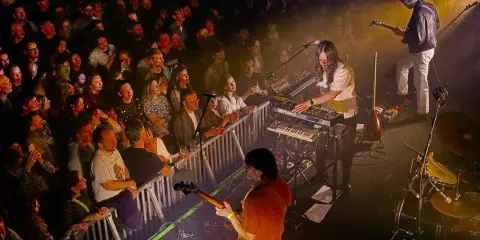 Publik njuter av Altin Gün i Stockholm. En gitarrist spelar, en keyboardist bakom Roland-syntar, och en entusiastisk publik bakom stängsel.