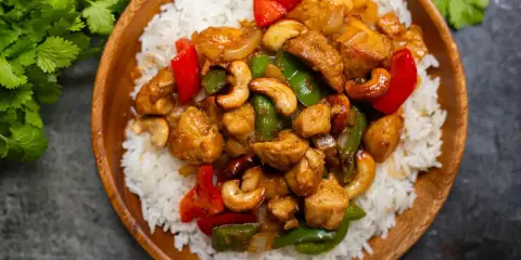Un délicieux poulet noix de cajou servi sur un lit de riz blanc. Des poivrons rouges et verts ajoutent de la couleur à ce plat savoureux.