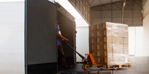 Un operario usa una carretilla para el transporte de materiales, cargando cajas en un camión.