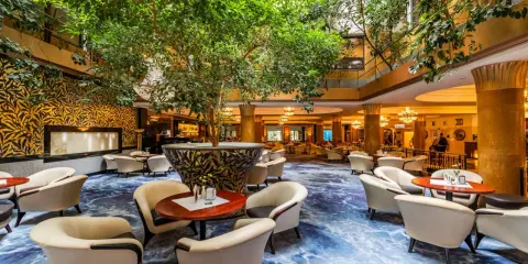 Luksusowy hol hotelowy z bujną roślinnością, wygodnymi fotelami i ozdobnym dywanem. Idealne miejsce na relaks w sieci luksusowych hoteli.