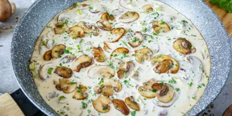 Cremige Rahmsauce mit frischen Champignons, verfeinert mit Petersilie, in einer Pfanne.