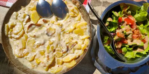 Plat de pommes de terre crémeuses, une spécialité auvergnate, servi dans une poêle avec une salade fraîche.
