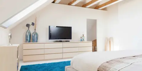 Schlafzimmer im Dachgeschoss, ideal zum Dachboden ausbauen. Helle Farben, Holzbalken und ein blauer Teppich schaffen Gemütlichkeit.