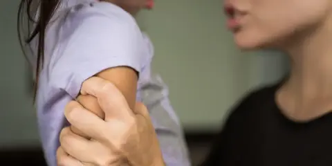 Eine Erzieherin hält ein Kind am Arm fest, während sie spricht. Die Frage, ob eine Erzieherin ein Kind festhalten darf, ist komplex.