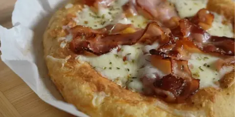 Pyszna pizza z mozzarellą i chrupiącym boczkiem, posypana ziołami. Idealna na szybki lunch.