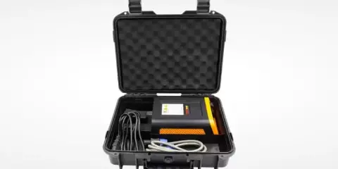 Estuche negro abierto con un dispositivo electrónico negro y naranja, cables y espuma protectora. Ideal para un sacabollos profesional.