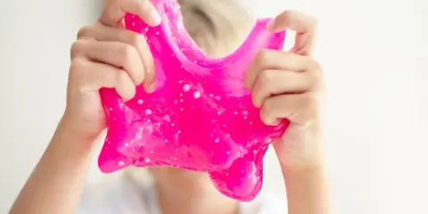 Dziecko bawi się różowym slime, który wygląda jak z przepisu na domowy slime.