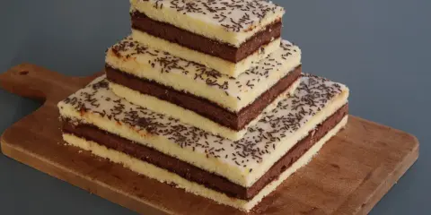 Trois parts de napolitain sans gluten empilées sur une planche en bois, garnies de vermicelles au chocolat.