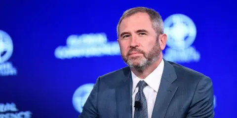 Brad Garlinghouse, CEO Ripple, w niebieskim garniturze, z brodą, na tle niebieskiej sceny z logo Global Conference.