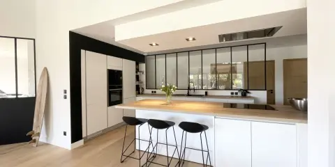 Cuisine moderne avec îlot central, plan de travail en bois et verrière industrielle. Une belle idée cuisine avec verriere pour un espace lumineux.