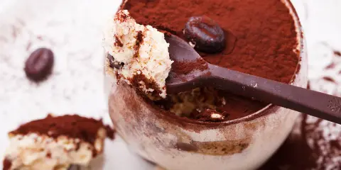 Un déliceux tiramisu cacao, saupoudré de cacao, avec une cuillère pleine de crème onctueuse et un grain de café.