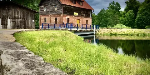 Stara ceglana budowla nad jeziorem Cekcyn, z drewnianą przybudówką i pomostem.