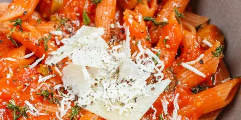Penne w sosie pomidorowym z oliwkami i parmezanem. Idealny szybki obiad z makaronem, doprawiony ziołami.