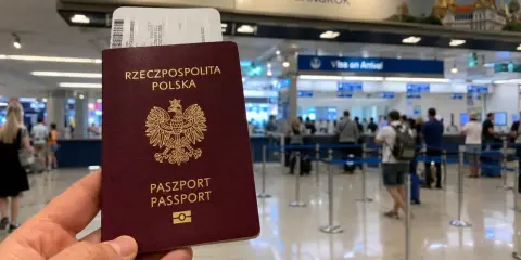 Polski paszport i bilet lotniczy w ręku, w tle tablica "THAILAND BANGKOK" i stanowiska "Visa on Arrival". Sprawdzanie tajlandia warunki wjazdu.