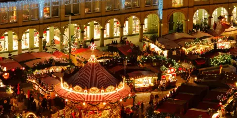 Mercadillos navideños España: un carrusel iluminado y puestos de madera bajo luces festivas, creando un ambiente mágico.