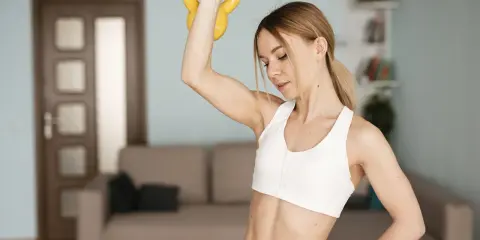 Kobieta wykonuje ćwiczenia na smukłe ramiona z kettlebell w domu.