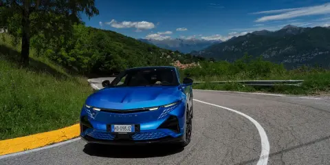 L'Alpine A290 sfreccia su una strada di montagna panoramica, con un cielo azzurro e montagne sullo sfondo.
