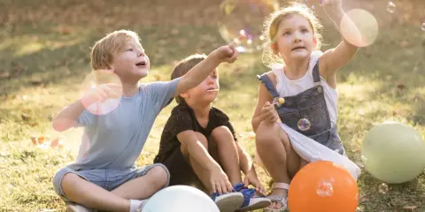 Trójka dzieci cieszy się bańkami mydlanymi na trawie. Radosne zabawy na polu w słoneczny dzień.