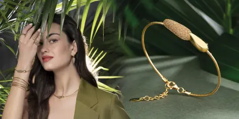 Modella con gioielli Pesavento, tra cui una collana, orecchini e anelli, su sfondo verde con foglie tropicali.