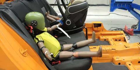 Maniquíes en un asiento de coche de prueba, preparándose para un test de seguridad según la normativa ECE R44/04.