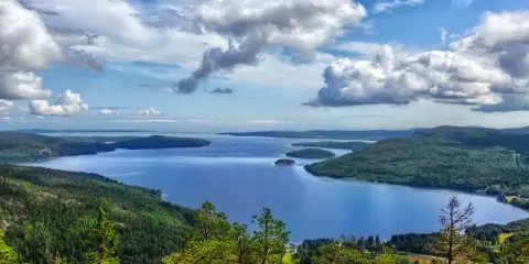 Vacker utsikt över en sjö med öar, omgiven av skogklädda berg. Ett perfekt ställe att uppleva Stockholms naturreservat.