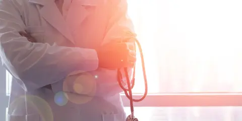 Lekarz w białym kitlu trzyma stetoskop. W tle okno z widokiem na miasto. To symbol najlepszych hematologów w Polsce.