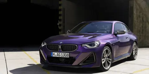 Fioletowe BMW 220i coupe z nowoczesnym designem, zaparkowane na betonowym placu przed ciemnym budynkiem.