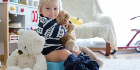 Chłopiec na nocniku, przytulający misia. To jego skok rozwojowy 18 miesiąc. Obok siedzi drugi miś.